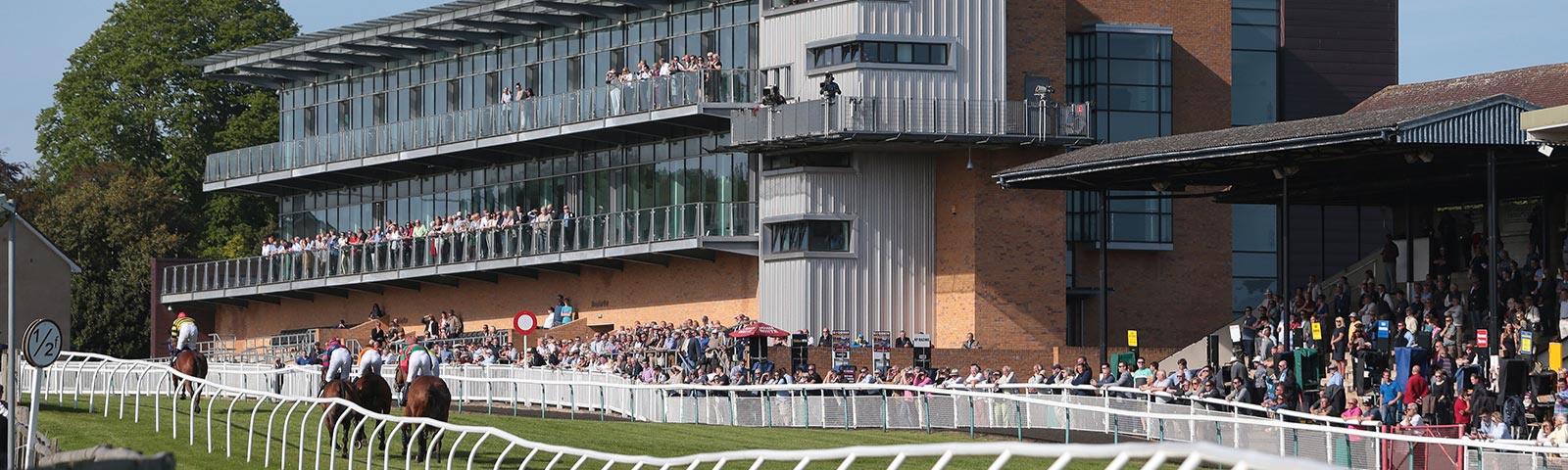 Crowds watching racing at Fontwell Park Racecourse, with the main grandstand building in the background.