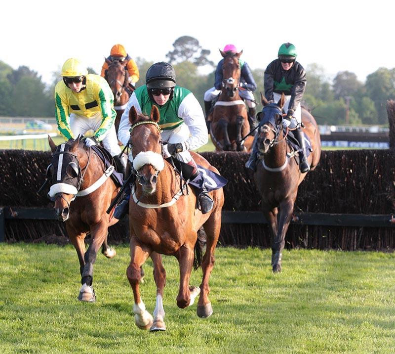 Group of jockeys racing at Fontwell Park Racecourse with few of them jumping over a hurdle.